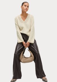 Maglione lavorato a maglia di colore crema con scollo a V e dettagli a occhiello, abbinato a pantaloni in pelle marrone scuro a gamba larga a vita alta e una borsa beige.