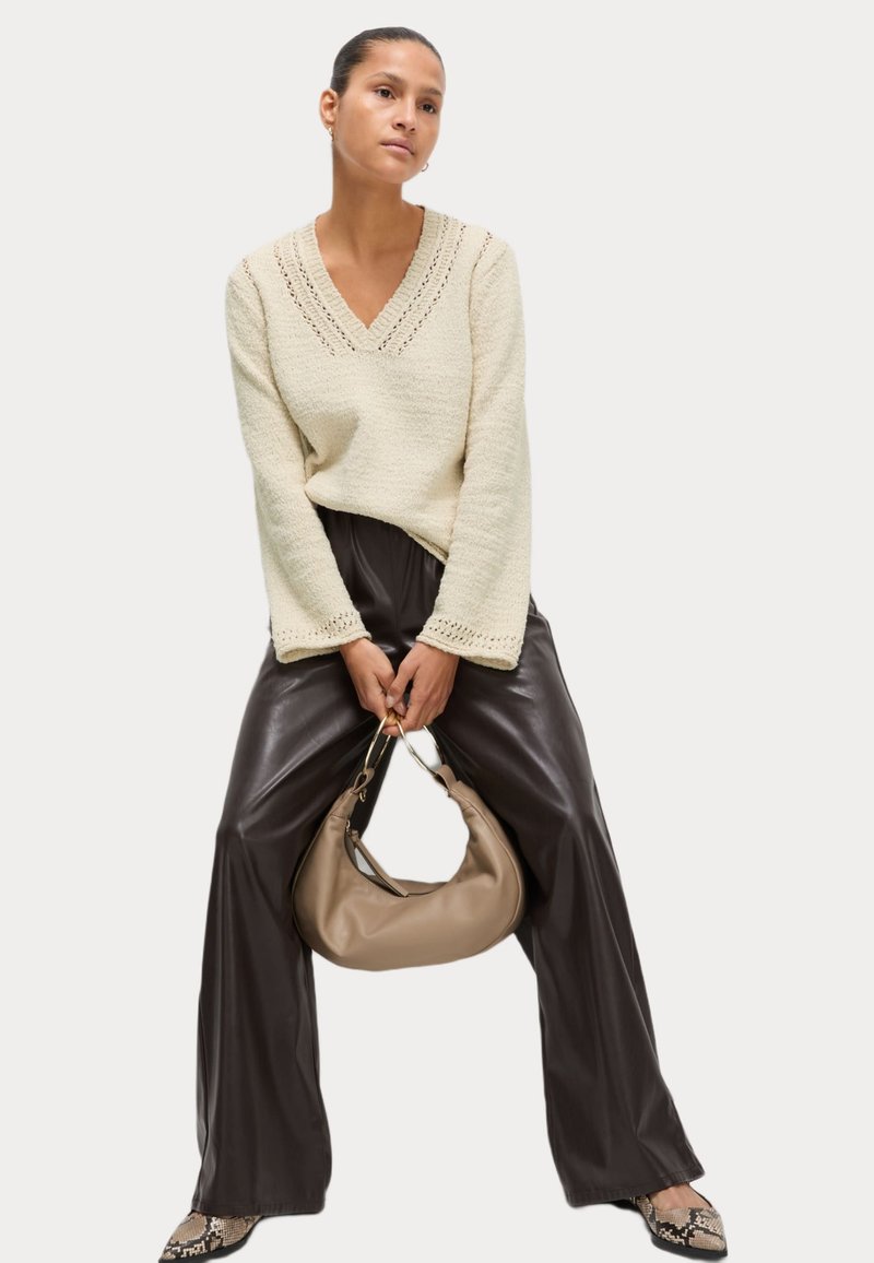 Maglione lavorato a maglia di colore crema con scollo a V e dettagli a occhiello, abbinato a pantaloni in pelle marrone scuro a gamba larga a vita alta e una borsa beige.