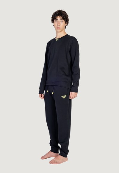 Completo felpa nera e pantaloni in tessuto morbido, con un logo giallo sul petto e un dettaglio giallo sui pantaloni. Entrambi hanno una vestibilità rilassata.