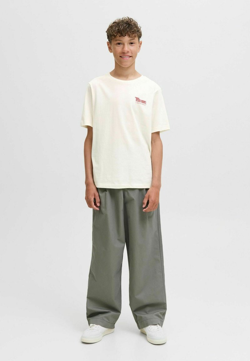 Voľný svetlofialový tričko s červeným logom, spárované s veľkými šedými nohavicami a bielymi teniskami. Neformálny, uvoľnený outfit.