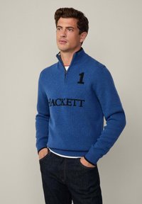 Suéter azul de lana con cremallera y puños y dobladillo acanalados. Presenta el logo negro "HACKETT" y el número "1" en el frente. Diseño informal.