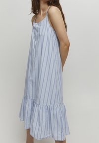 Blå och vit randig ärmlös klänning med volangkant, tillverkad av lätt tyg, med tunna remmar och avslappnad passform.