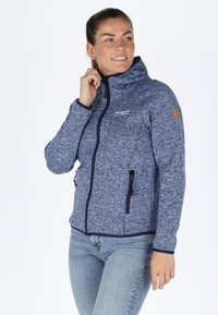 Giacca in pile blu navy con colletto alto, frontale con zip e due tasche laterali. Presenta un motivo a maglia testurizzata e un logo sul petto.