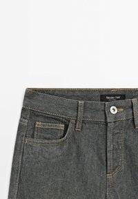 Donkerblauwe spijkerbroek met een klassieke vijf-pocketontwerp, contrasterende tan stiksels, een metalen knoop en een label met de tekst "Massimo Dutti."