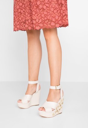 Legs wearing coral lace skirt and cream wedge sandals with ankle straps and gold butterfly embellishments on the heels.
