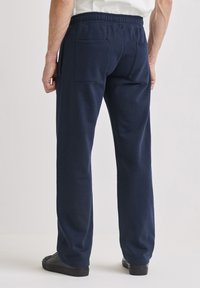 Tummansiniset collegehousut, joissa on kuminauhavyötärö, kaksi takataskua, rento istuvuus ja sileä pinta.