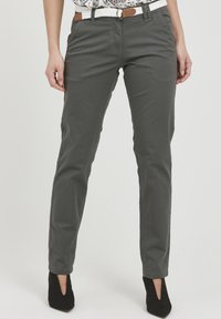 Pantalons gris en mélange de coton avec une coupe slim, dotés de poches avant et d'une ceinture marron. Portés avec des chaussures à talons noires. Texture unie.