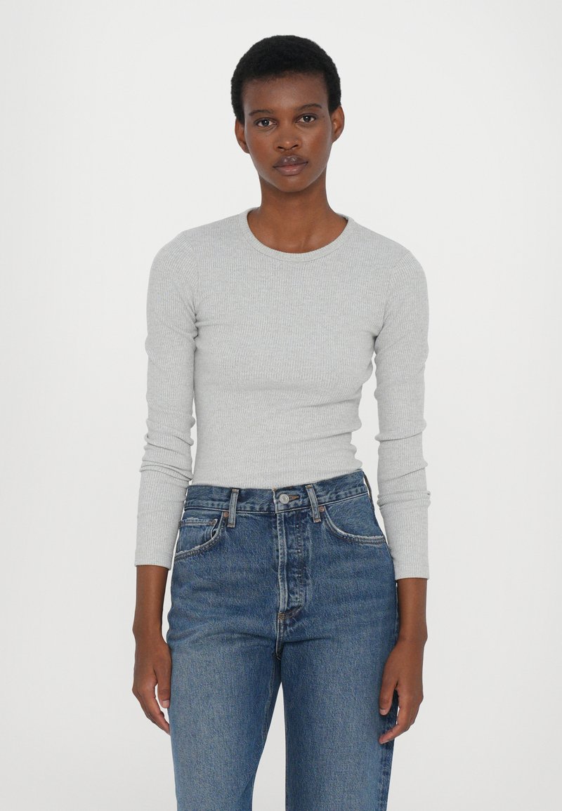 Long-sleeve, light gray ribbed top with a round neckline, paired with high-waisted, medium blue denim jeans with a classic button fly.