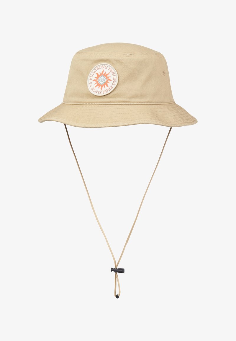 Μπεζ καπέλο κουβάς με φαρδύ γείσο, ρυθμιζόμενο λουράκι κάτω από το πηγούνι και στρογγυλό πατς με ήλιο και κείμενο στη μπροστινή πλευρά.