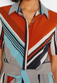 Chemise à boutons avec un col classique, présentant des rayures diagonales audacieuses en orange, bleu, gris et crème ; comprend un détail de taille nouée.