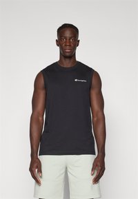Camiseta de algodón negra sin mangas con cuello redondo y pequeño logotipo bordado en blanco en el pecho, combinada con pantalones cortos verde claro.