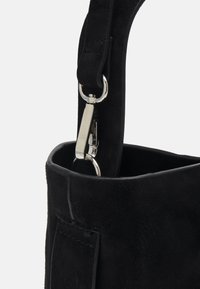 Bandoulière en suède noir fixée par un fermoir pivotant en métal argenté à un bord assorti d'un sac en suède noir.