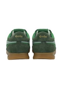 Un paio di sneaker verde scamosciato e tessuto con suole marroni, viste da dietro, con il logo "Gola" in oro su ciascun tallone.