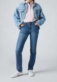 Jean en denim bleu avec une coupe droite, assorti à une veste en denim bleu clair oversize et une chemise à rayures rose et blanche. Baskets blanches.