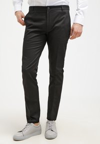 Svarta skräddarsydda byxor med smal passform, slät yta och subtil lyster, i kombination med ljusgrå avslappnade sneakers.