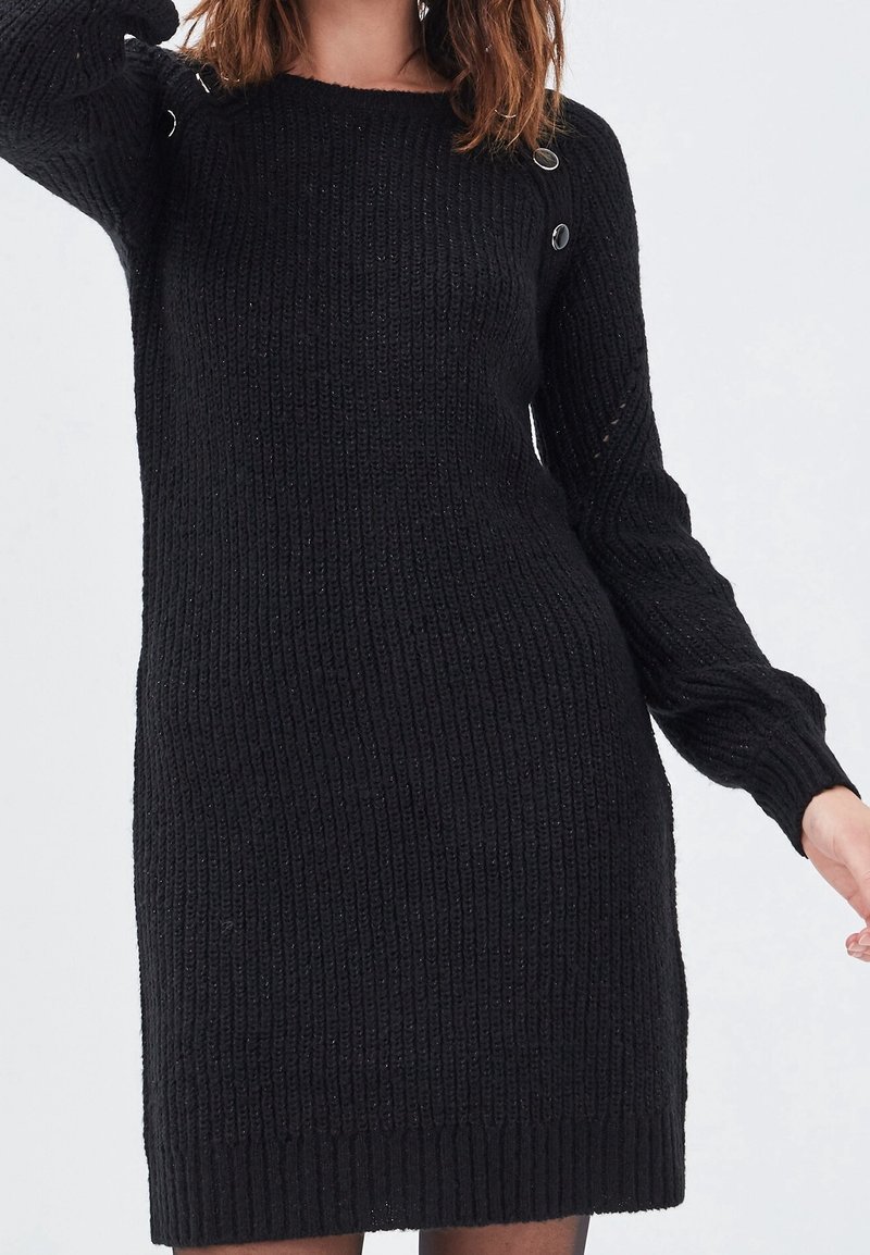 Robe noire tricotée avec texture côtelée, manches longues et boutons décoratifs sur l'épaule. Coupe lisse et décontractée jusqu'aux genoux.