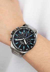 Orologio in acciaio inossidabile argentato con quadrante nero, tre sotto-quadranti, accenti blu e scala tachimetrica sulla lunetta. Bracciale a maglie metalliche.