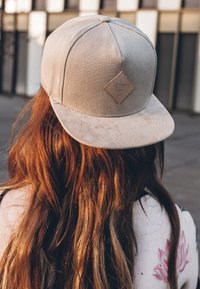 Beige baseball sapka, texturált anyagból, gyémánt alakú logóval ellátott folttal és ívelt perímmel, hátulról nézve.