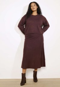 Burgundijas krāsas adīta divdaļīgā komplekta tērps, kas sastāv no īsa džempera un garās svārku. Mīksta tekstūra ar nelielu mirdzumu, kombinācijā ar brūnām potīšu zābakiem.