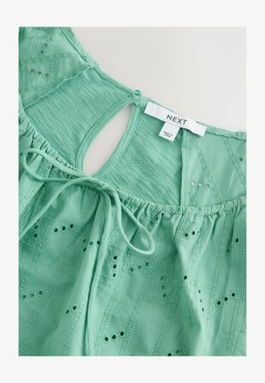 Mintgroene top met textuurdetails, voorzien van geborduurde patronen en een gestrikte tailleband. Sleutelgat achterdesign met label zichtbaar.