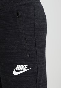 Gros plan sur un pantalon de survêtement noir Nike montrant une poche zippée et le logo Nike blanc sur un tissu texturé.