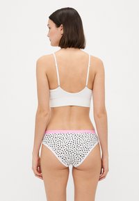 Bralet alb cu bretele ajustabile, asociat cu chiloți hipster cu buline și o talie roz, toate realizate dintr-un material elastic.
