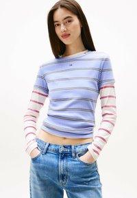 Lichtblauwe geribbelde top met lange mouwen en horizontale strepen in rood en wit. Gecombineerd met hooggewaisted blauwe jeans.