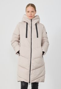 Lys beige pufferjakke med hette, frontglidelås og sorte snorer. Har skrå quilting og sidelommer; glatt tekstur.
