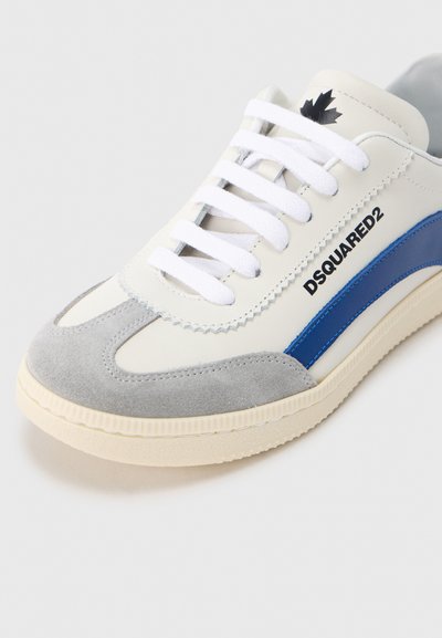 Άσπρο αθλητικό παπούτσι με γκρι και μπλε λεπτομέρειες, κατασκευασμένο από δέρμα και σουέντ. Διαθέτει λευκά κορδόνια, υφασμένη σόλα και μαύρο λογότυπο στο πλάι.