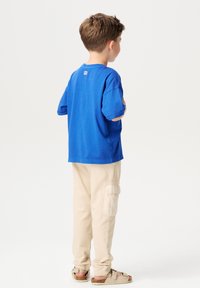 Blauwe katoenen T-shirt met korte mouwen, gecombineerd met beige cargobroek met zijzakken en bruine sandalen met banden.