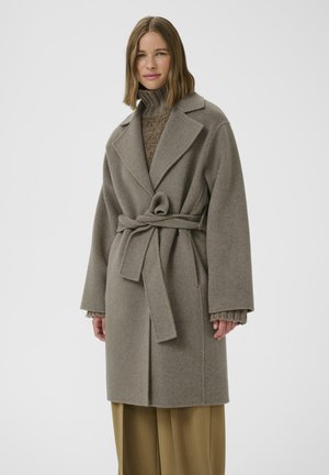 Light gray wool coat with a belted waist, large lapels, and wide sleeves, layered over a textured brown sweater and loose beige trousers.