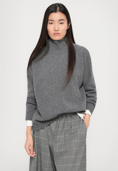 Grauer, gestrickter Rollkragenpullover mit geripptem Ausschnitt und lockerer Passform, kombiniert mit grauen, karierte weit geschnittenen Hosen, die eine weiche Textur zeigen.
