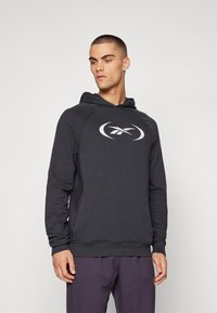 Haut à capuche gris foncé en tissu doux, arborant un grand logo blanc sur le devant, avec une poche kangourou et des poignets et un ourlet côtelés.
