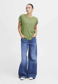 Camiseta verde de manga corta con escote redondo combinada con vaqueros azules de talle alto y pierna ancha. Calzado casual completa el conjunto.