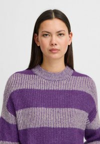 Violet un krēmkrāsas svītrainā džemperis ar ribotu struktūru, apaļu kaklu un brīvu piegriezumu. Izstrādāts ar plašām horizontālām svītrām.