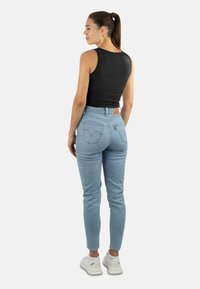 High-waisted light blue jeans with a fitted design, back pockets, and a leather patch at the waist, paired with a black sleeveless top.