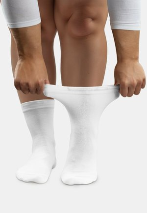 White cotton socks being pulled over feet, featuring a ribbed texture and a classic crew length, with a smooth fabric finish.