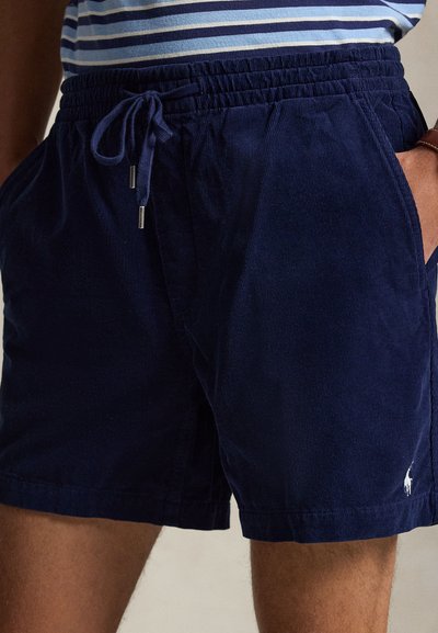 Short en velours côtelé bleu marine avec cordon de serrage et poches latérales, porté par une personne portant une chemise rayée.