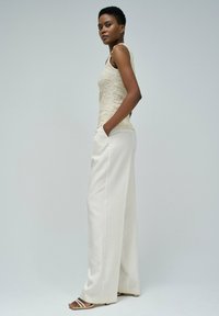 Top de tirantes de encaje en color beige claro combinado con pantalones anchos blancos con bolsillos. Sandalias deslizables con tiras delgadas completan el atuendo.