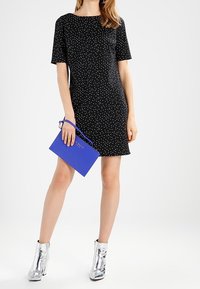 Černé šaty s krátkým rukávem a bílými puntíky, doplněné modrou kabelkou a stříbrnými metalickými kotníkovými botami.