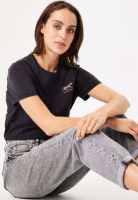 Camiseta de algodón negra con mangas cortas y un gráfico de tigre bordado en dorado. Combinada con jeans de mezclilla claros y enrollados.