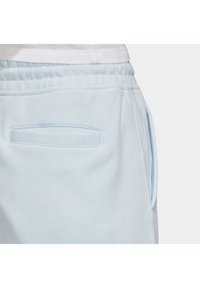 Ljusblå träningsoverall med en slät tygtextur, elastisk midja och sidofickor med subtil sömdekoration.