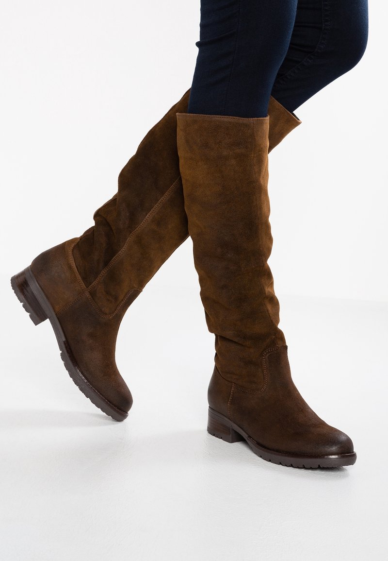 Bottes en suède marron au-dessus du genou avec un design décontracté, bout arrondi et un petit talon empilé. Tige texturée et finition lisse.