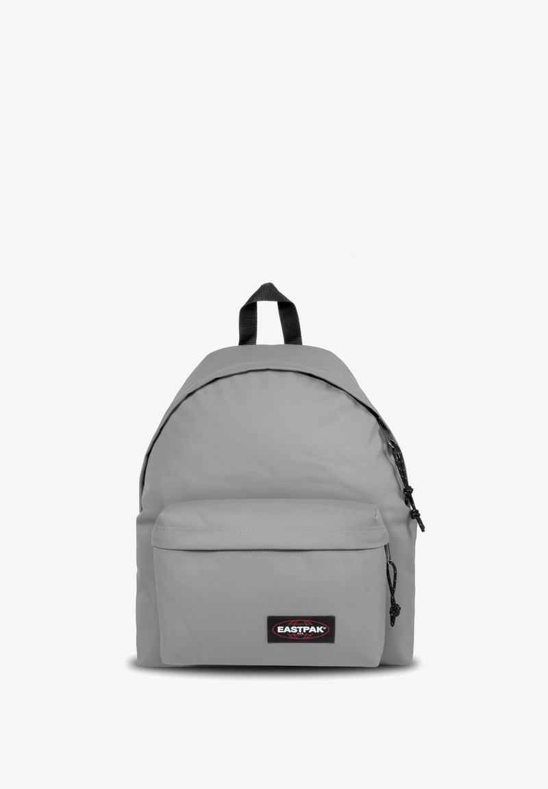 Sac à dos en tissu gris de forme arrondie, poche avant zippée et poignée supérieure. Il présente un patch logo et des accents noirs, avec des bretelles robustes.