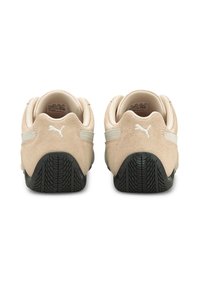 Baskets en daim beige avec une semelle extérieure en caoutchouc noir texturé et des accents rayés blancs sur les côtés. Vue arrière montrant le détail du logo.