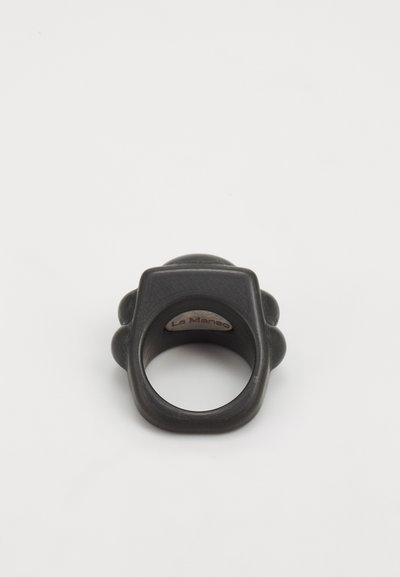 Black rubber ring with a rounded top and side accents. Features a smooth texture and a small logo visible on the inner band.