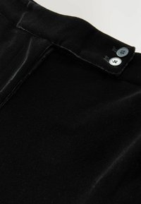 Tessuto di velluto nero con una texture liscia e una leggera lucentezza, con due dettagli di bottoni argento in vita.