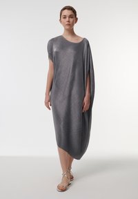 Vestido metálico gris, de largo hasta la rodilla, con diseño asimétrico, mangas anchas y textura suave. Combinado con sandalias plateadas de tiras.