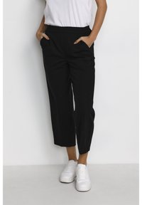 Pantalons noirs courts au tissu lisse, dotés de poches latérales et d'une taille haute, associés à des baskets blanches.