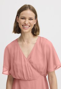 Robe rose avec des manches courtes et fluides et un décolleté en V. Fabriquée en tissu doux et léger avec une texture subtile et des drapés.